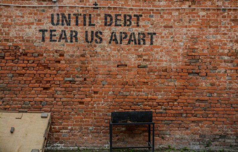 Debt Consolidation - Until debt tear us apart printed red brick wall at daytime