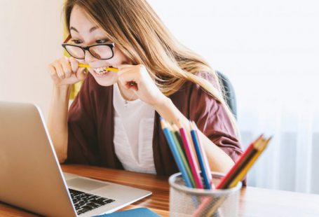 Student Loans - woman biting pencil while sitting on chair in front of computer during daytime