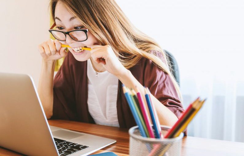 Student Loans - woman biting pencil while sitting on chair in front of computer during daytime