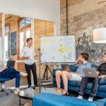 Robo-advisor - three men sitting while using laptops and watching man beside whiteboard