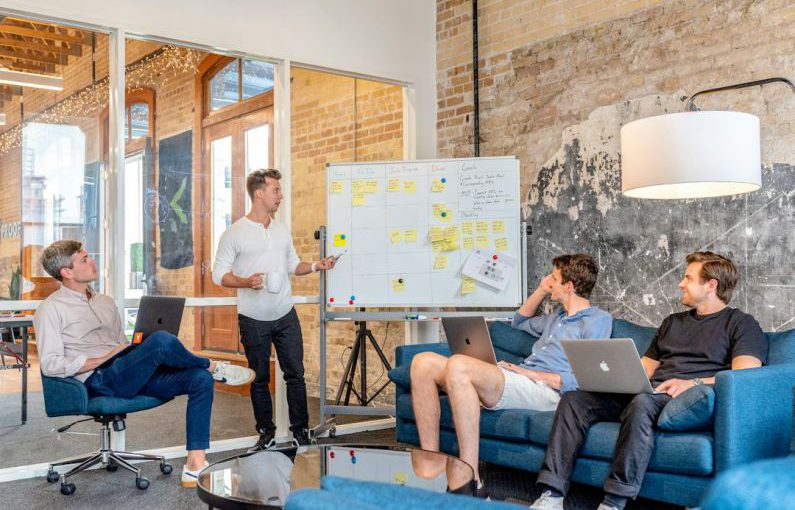 Robo-advisor - three men sitting while using laptops and watching man beside whiteboard